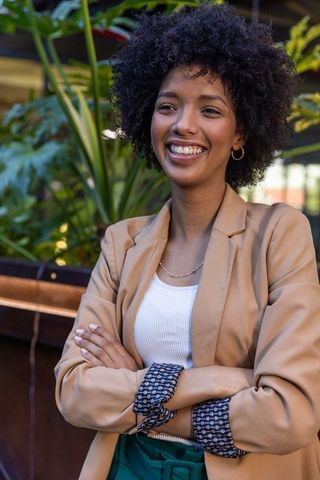 Confident Businesswoman Leaning at Sunlit Café Patio with Greenery