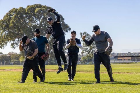Multiethnic baseball team leaping and walking across outfield celebrating team camaraderie