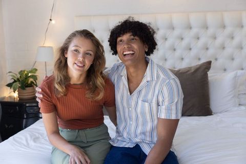 Young couple sitting on bed smiling embracing in cozy sunlit bedroom