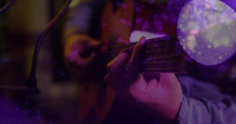 Playing acoustic guitar close-up with moody purple bokeh and intimate studio vibe
