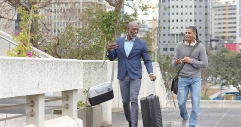 Diverse Colleagues Walking and Talking Through Urban Plaza With Suitcase and Duffel