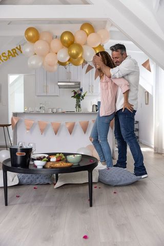 Couple celebrating anniversary at home with gold and blush balloons and cozy snacks