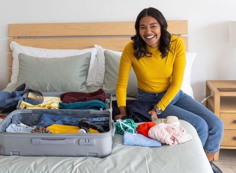 Smiling woman packing suitcase on bed for weekend travel and fitness trip