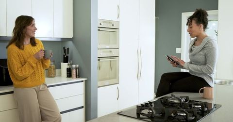Mid-adult friends chatting over mugs in modern minimalist kitchen, casual lifestyle