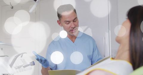 Dentist in blue scrubs explaining treatment plan while holding yellow chart to patient