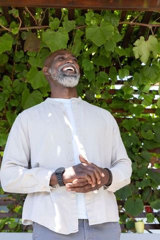 Senior african man laughing under pergola with lush vine leaves and sunlight