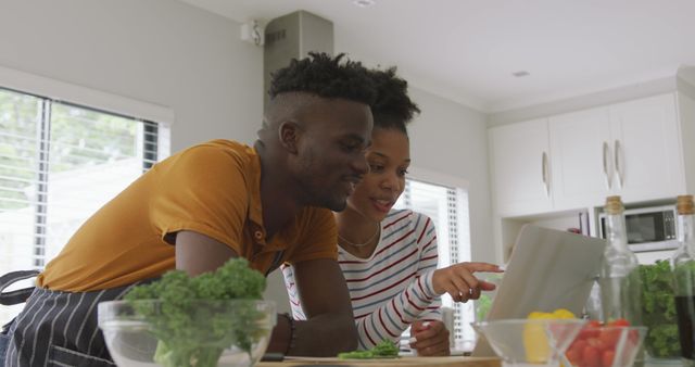 Image of happy african american couple cooking together in kitchen with tablet. love, relationship, togetherness and spending quality time at home.