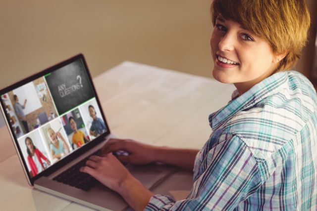 A young woman is participating in a virtual meeting using her laptop. She is smiling while interacting with other people in the online meeting. This image is ideal for illustrating concepts related to digital communication, remote working, online education, and virtual social interactions.