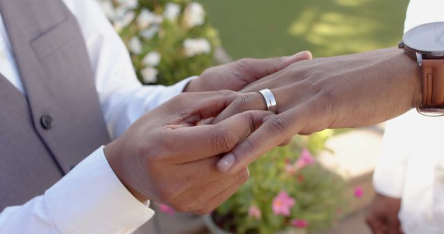This close-up shows a man placing a ring on his partner's finger during a wedding ceremony. Perfect for content related to weddings, engagements, love, romance, commitment, same-sex marriage, and celebratory events. Useful for wedding planning websites, love and relationship blogs, or articles focused on marriage equality.