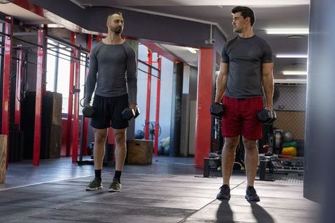 Two male training partners holding dumbbells in industrial gym lifting together by red rig