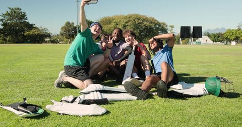 Youth cricket team taking selfie on sunny field with bat and pads showing camaraderie