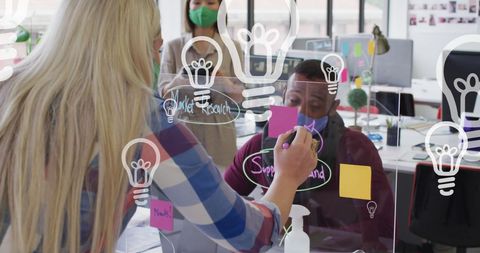 Diverse team of business professionals working together in an office. Wearing face masks for safety, they are brainstorming on various business strategies and digital media concepts. Ideal for illustrating teamwork, innovation, and safe business practices post-pandemic. Can be used in articles or promotions highlighting modern office environments or creative processes.