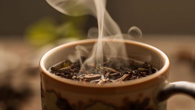 Steaming ceramic mug with loose leaf tea on wooden table evoking warm cozy morning