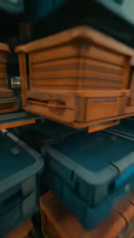 Vertical moving shot toward stacked orange and blue storage cases in busy warehouse aisle