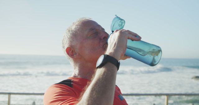 Senior caucasian man drinking water on promenade at seaside. Retirement, active lifestyle, summer and drink, unaltered.