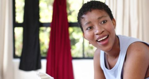 Young african american woman laughing leaning by window with red and black drapes