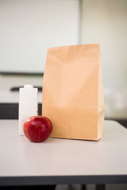 Close-up of apple with drink bottle and paper bag on table in classroom