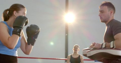Female Boxer Training with Coach Holding Focus Mitts in Ring with Dramatic Lens Flare