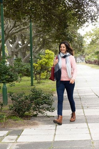 Woman walking on urban park pathway wearing pink cable knit sweater, scarf and leather boots