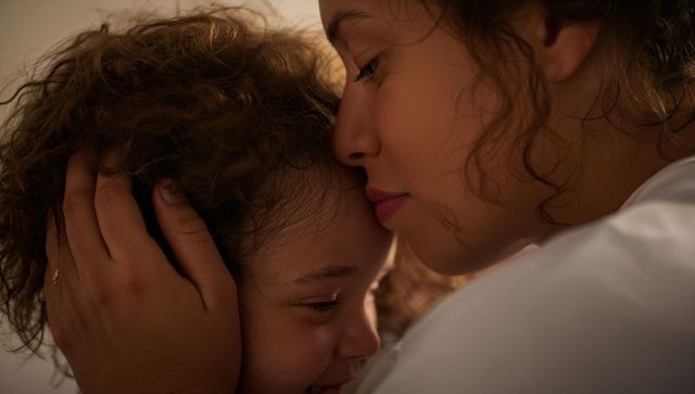 Mother cradling child closeup embrace showing curly hair small ring warm soft light
