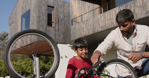 Father Teaching Son to Repair Bicycle Outside Modern Home