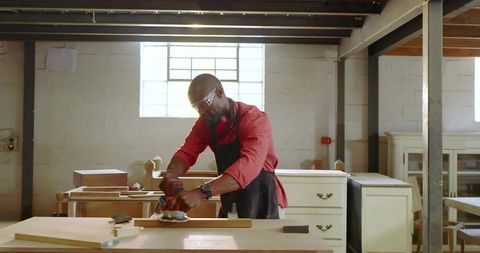 Experienced carpenter sanding wooden plank in rustic workshop, woodworking craftsmanship