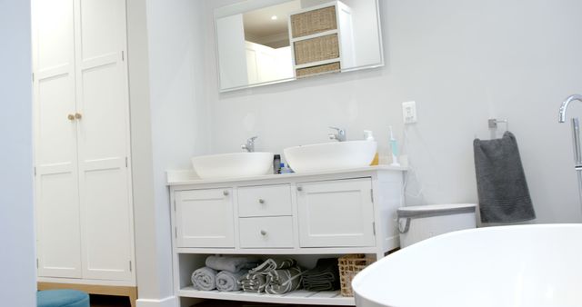 This image showcases a modern white bathroom featuring a double sink vanity and a freestanding bathtub. The clean and organized space includes neatly arranged towels and storage baskets. Ideal for use in home decor blogs, interior design inspirations, real estate listings, and bathroom renovation brochures.