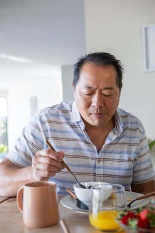 Mature Asian Man Enjoying Meal with Chopsticks at Bright Kitchen Table