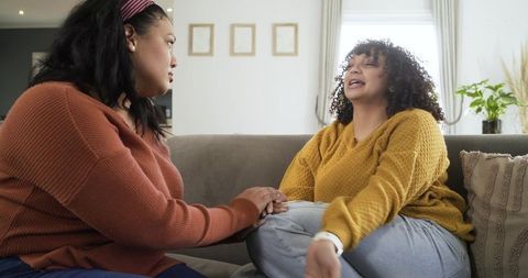 African american women holding hands and sharing emotional conversation on sofa at home