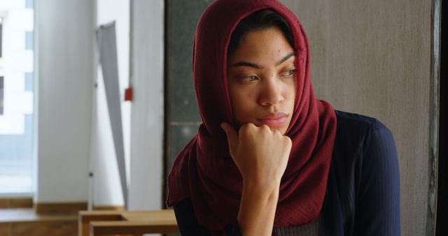 Pensive Woman in Red Hijab Sitting Indoors - Download Free Stock Images Pikwizard.com