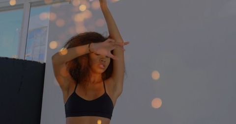 Stretching woman raising arm across face in minimalist studio with warm bokeh glow
