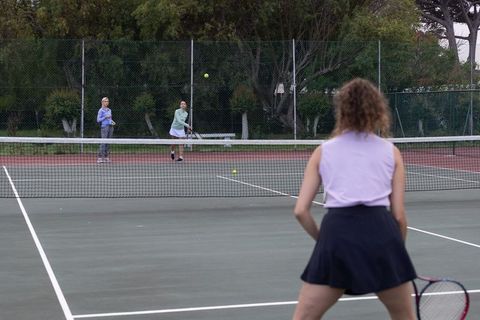 Women doubles tennis rally outdoor court overcast player in foreground returning ball