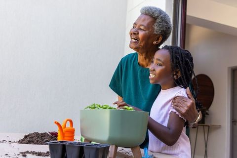 Smiling african american grandmother teaching granddaughter gardening with raised planter