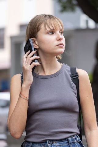 Young woman talking on smartphone while walking city sidewalk, casual urban style