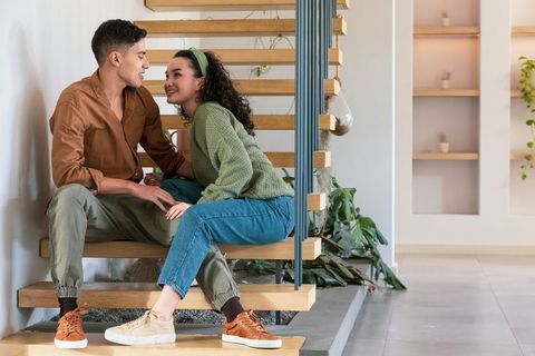 Asian couple sitting on floating wooden stairs sharing cozy moment with mug in modern home