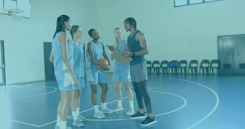 Coach huddling and instructing women's basketball team on indoor court during practice