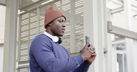 Urban commuter checking smartphone at transit shelter wearing beanie and headphones