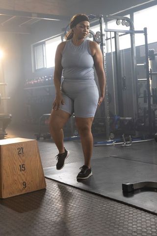 African american woman stepping onto plyo box during strength and cardio training in gym