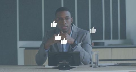 Executive businessman sitting at boardroom table clasping hands with tablet and like icons