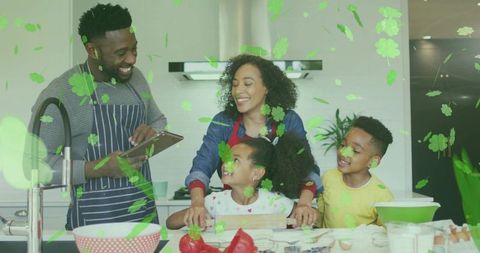 Family cooking together at kitchen island, father using tablet while kids helping and smiling