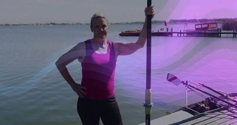 Woman athlete standing on dock by lake holding rowing oar