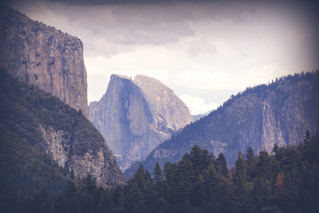 Majestic view of Yosemite Valley featuring Half Dome in the background and forested cliffs in the foreground under a moody sky. Ideal for use in travel guides, nature documentaries, environmental campaigns, and inspirational posters.
