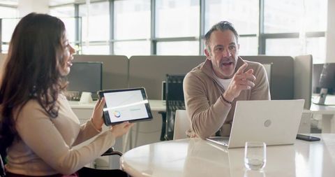 Diverse coworkers collaborating over tablet chart in modern open-plan office meeting