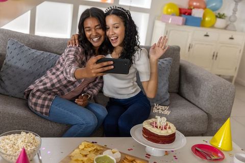 Mother and teenage daughter taking selfie while celebrating 18th birthday at home