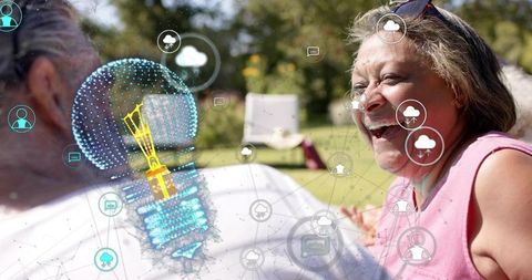 Senior woman laughing on sunlit lawn with partner and holographic lightbulb symbolic of smart living