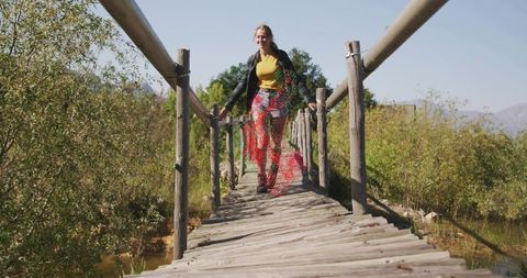 Woman hiking across rustic footbridge in scenic marsh landscape