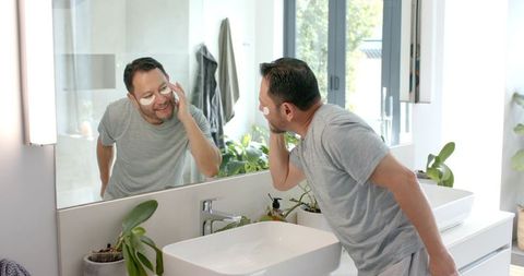 Man Engaged in Skincare Routine with Eye Patches Near Bathroom Mirror