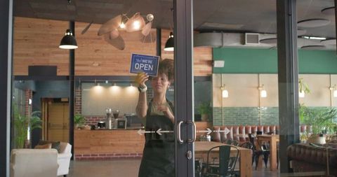 Barista placing open sign on glass doors of rustic industrial coffeehouse