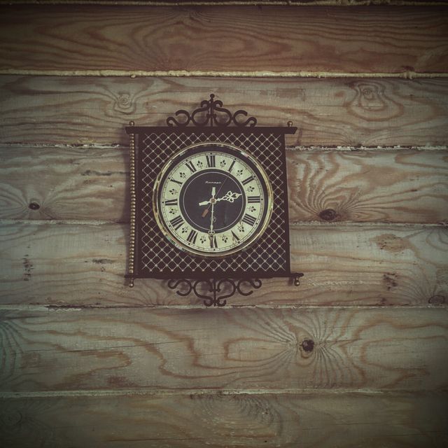 Vintage wall clock with Roman numerals hangs on a wooden wall, evoking a sense of nostalgia and rustic charm. Ideal for use in articles, advertisements, and blog posts about interior design, home decor, antiques, and rustic living. Perfect for illustrating themes of time, vintage style, and traditional craftsmanship.