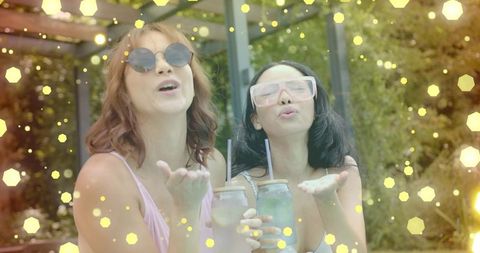 Blowing kisses under pergola, friends wearing sunglasses holding mason jar summer drinks